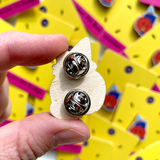 the rear of the pin badge is shown revealing two metal fasteners that stop it spinning